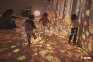 Bambini calciano le foglie d'autunno proiettate sul pavimento e afferrano quelle sulla parete nella stanza magica